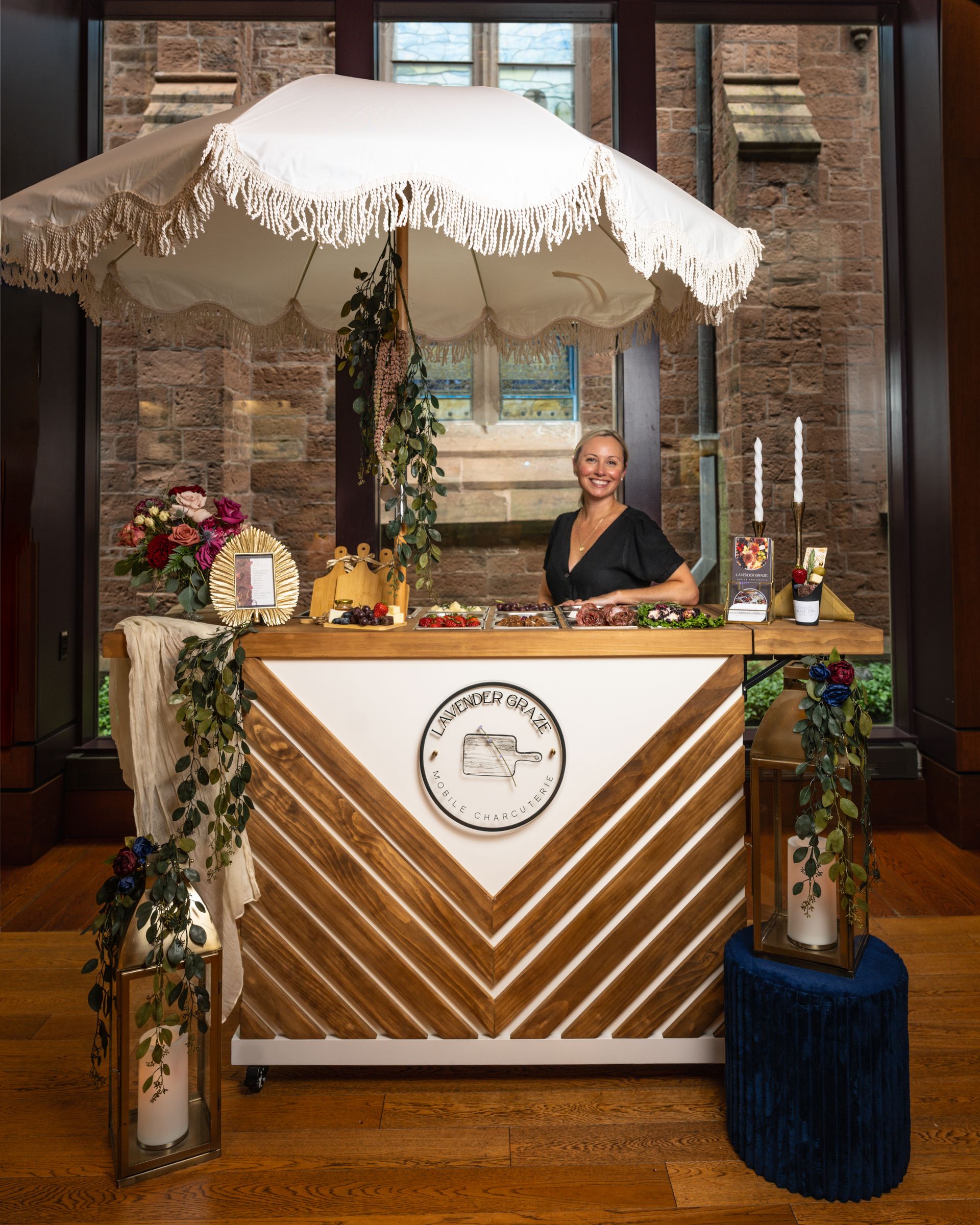 Woman behind a decorated market stall with striped front and white canopy in a brick-walled venue