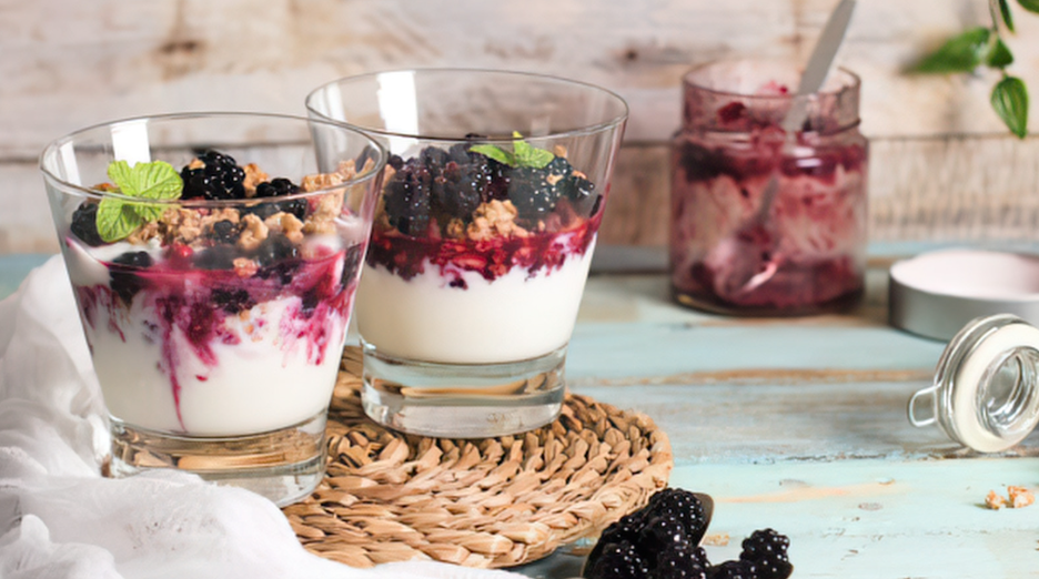 Berry parfaits in glasses with yogurt and granola on a rustic table, with a jar of berry jam nearby