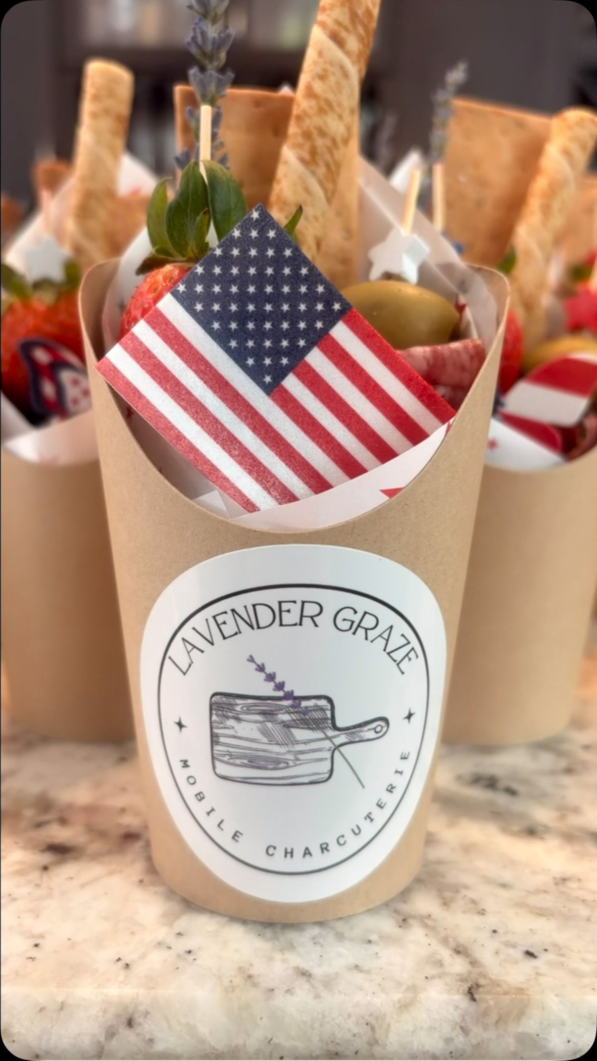 Gift cups with American flags and breadsticks on a countertop, with a lavender-themed label.