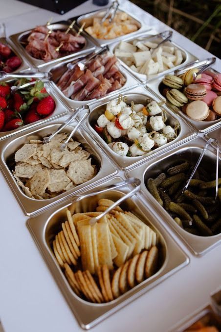 Assorted tapas in small foil trays, including olives, crackers, nuts, berries, and marinated vegetables.