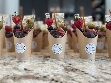 Rows of berry parfaits in kraft cups topped with strawberries and grapes on a marble counter