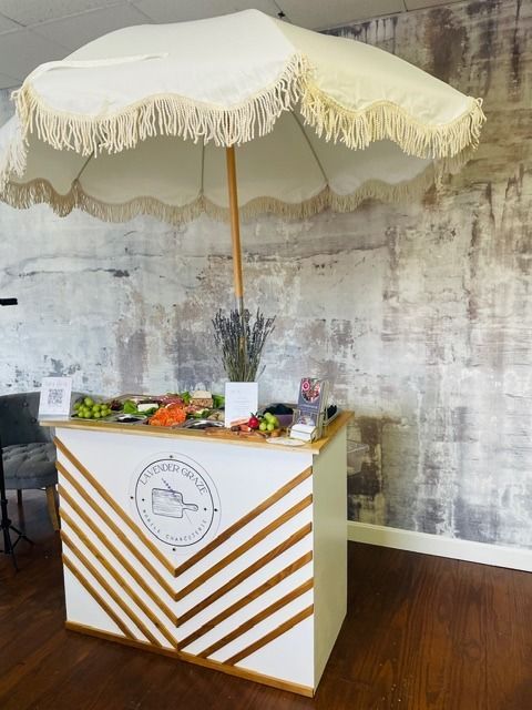 White fringed parasol over a striped display table with flowers in a rustic room, set against a weathered wall