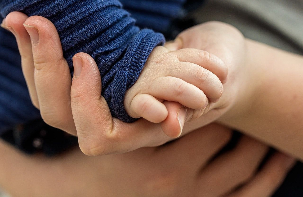 Adult hand gently holding a baby's hand, blue sleeve visible, close-up.