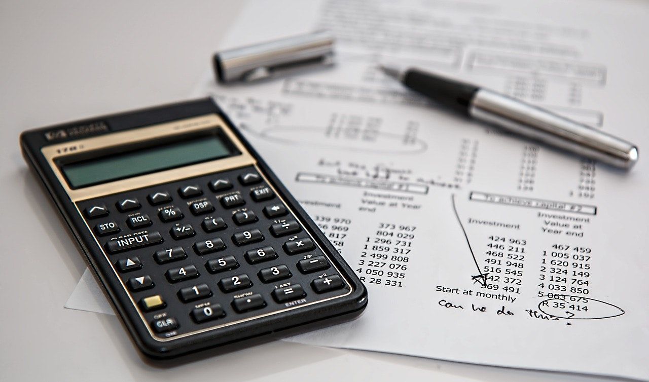Calculator, paperwork with handwritten notes, and pen on a white surface, suggesting financial calculations.
