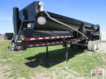 A black dump trailer is parked in a grassy field