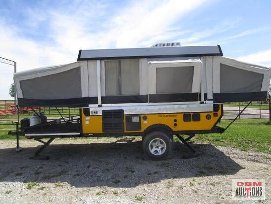 A yellow camper trailer is parked in a gravel lot.