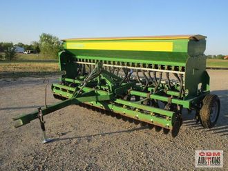 A green and yellow tractor is parked in a dirt field.
