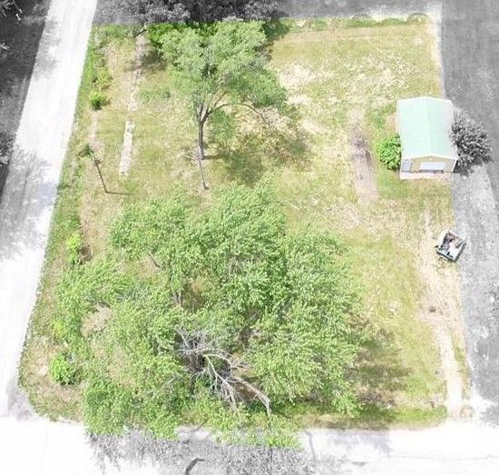 An aerial view of a grassy field with trees and a house in the background.