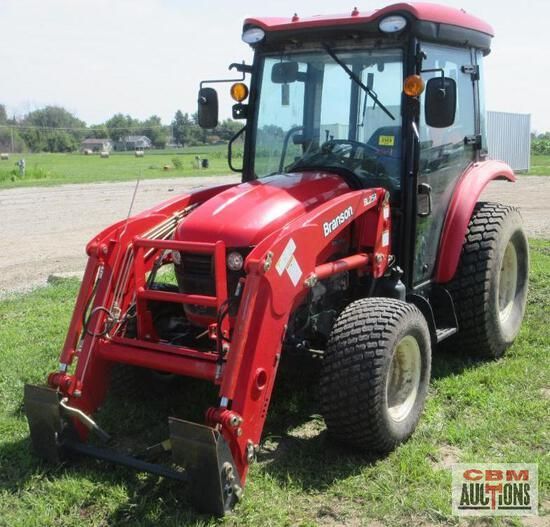 A red tractor is parked in a grassy field next to a cbm auction sign