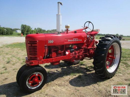 A red farmall tractor is parked in a dirt field