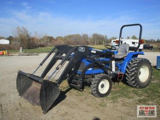 A blue tractor with a front loader is parked in a dirt lot.