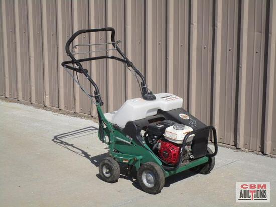A green and white lawn mower is parked in front of a building.