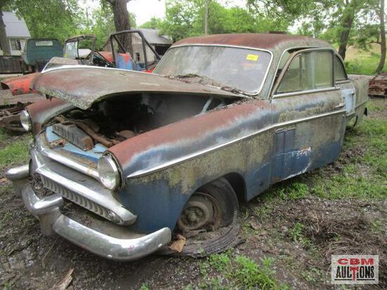 An old rusty car is sitting in the grass with its hood up.