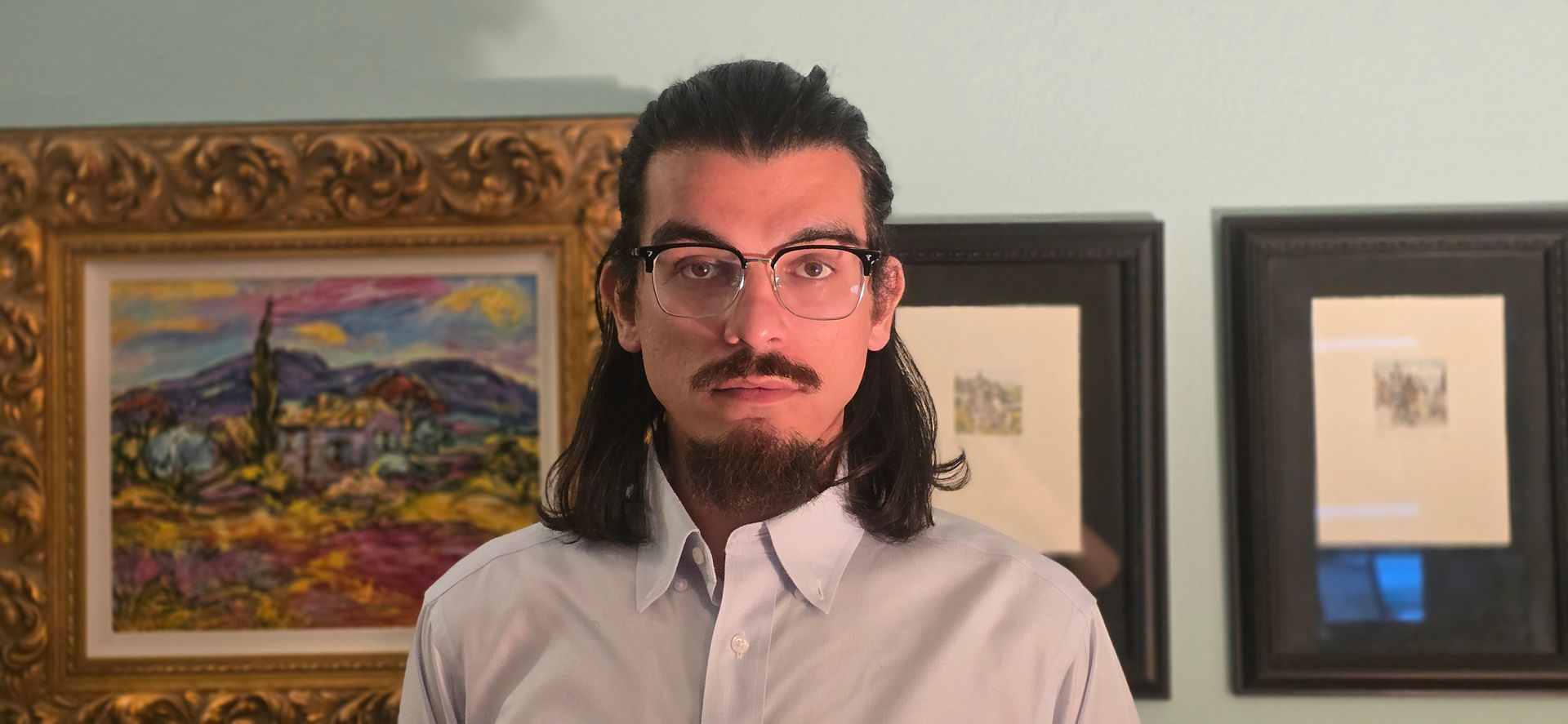 Owner of  Agency standing indoors in front of framed artwork, wearing glasses and a white shirt.