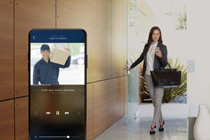 Woman in office hallway using smartphone app with delivery worker shown on screen