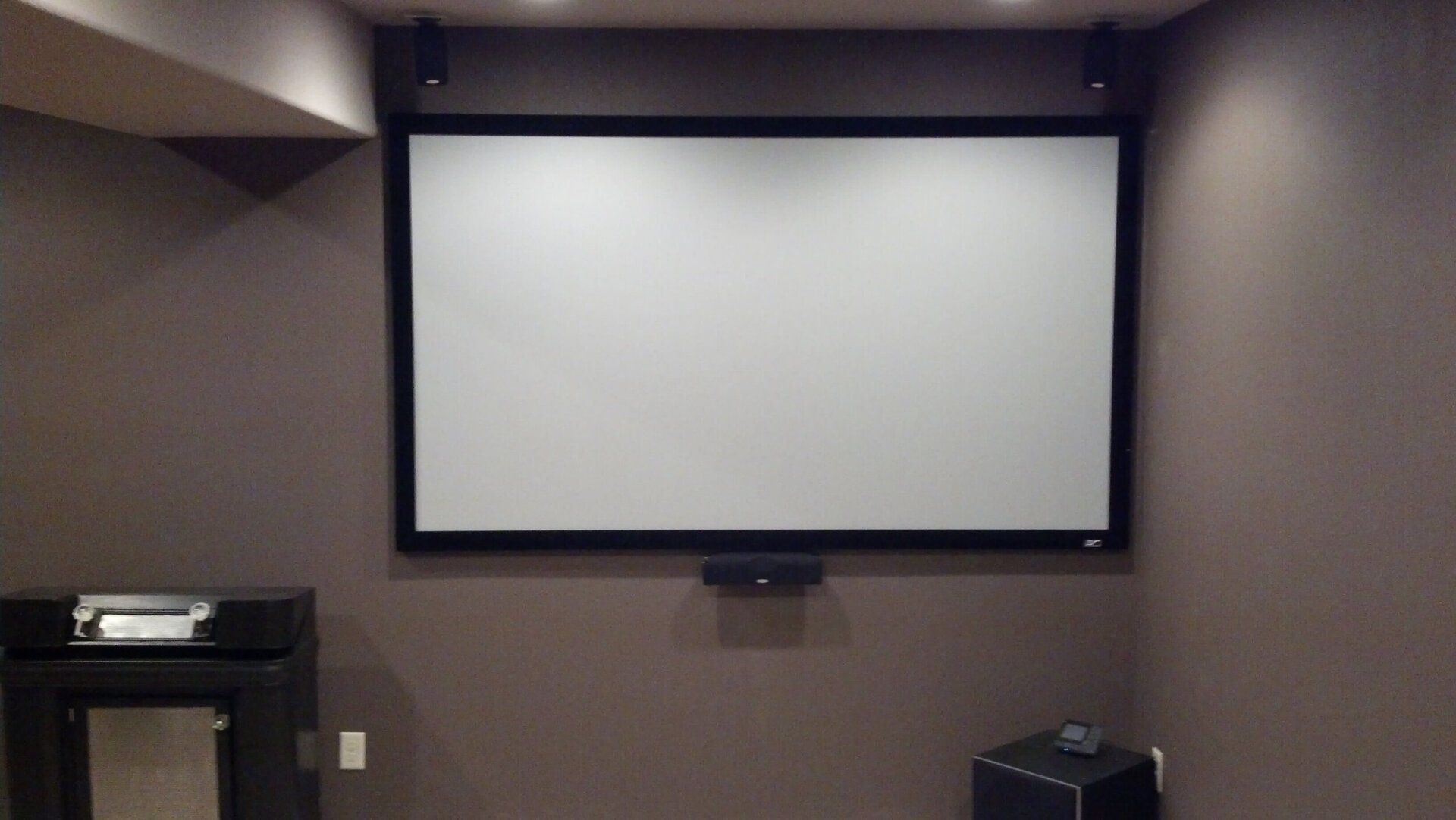Home theater room with a blank projection screen on a gray wall.