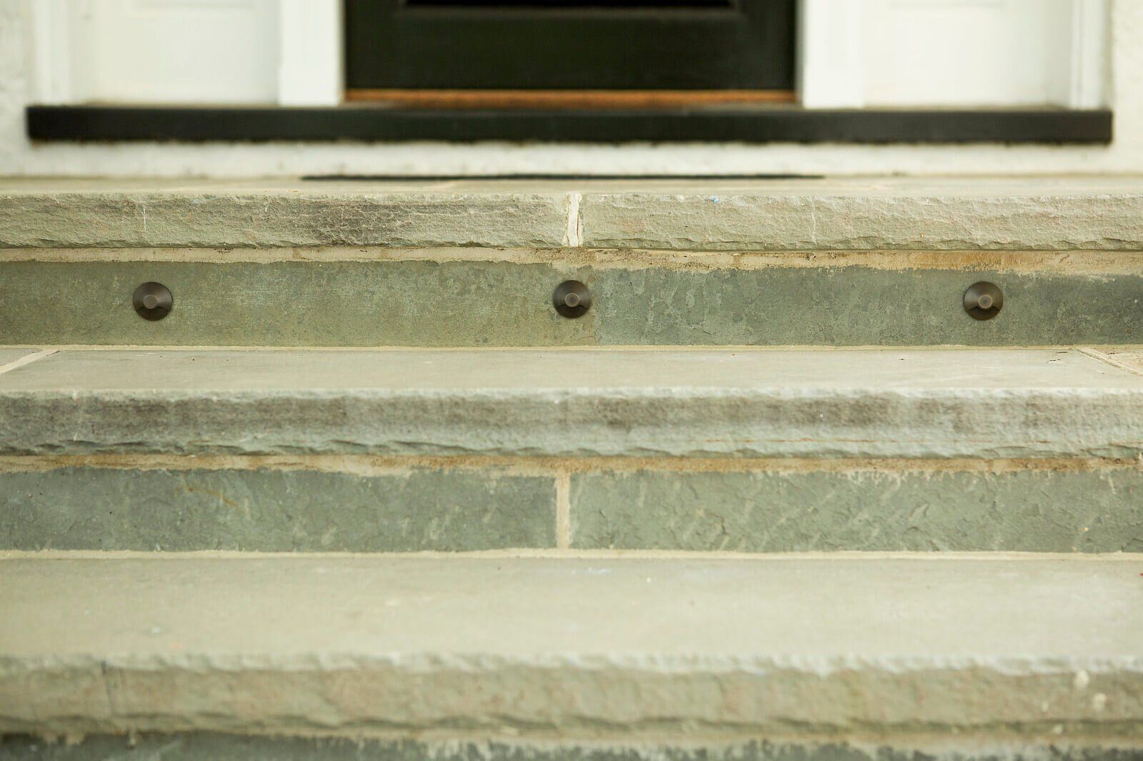 Weathered stone steps with three dark bolts beneath a window sill