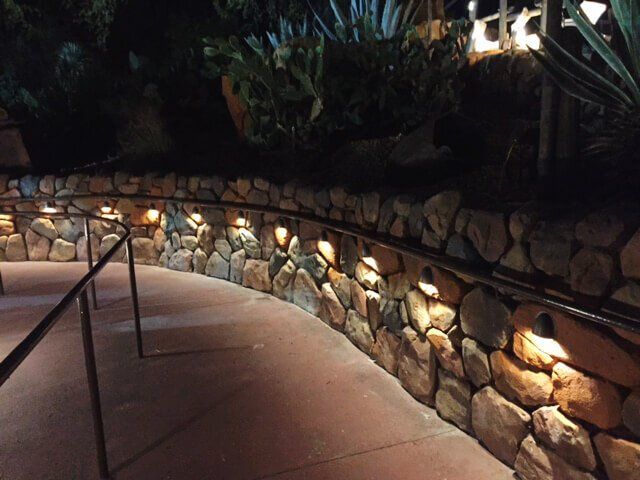 Stone retaining wall with warm lights along a curving outdoor walkway at night
