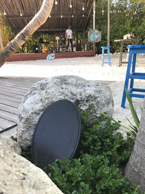 Outdoor seating area with large rocks, blue stools, and a wooden deck under a thatched roof