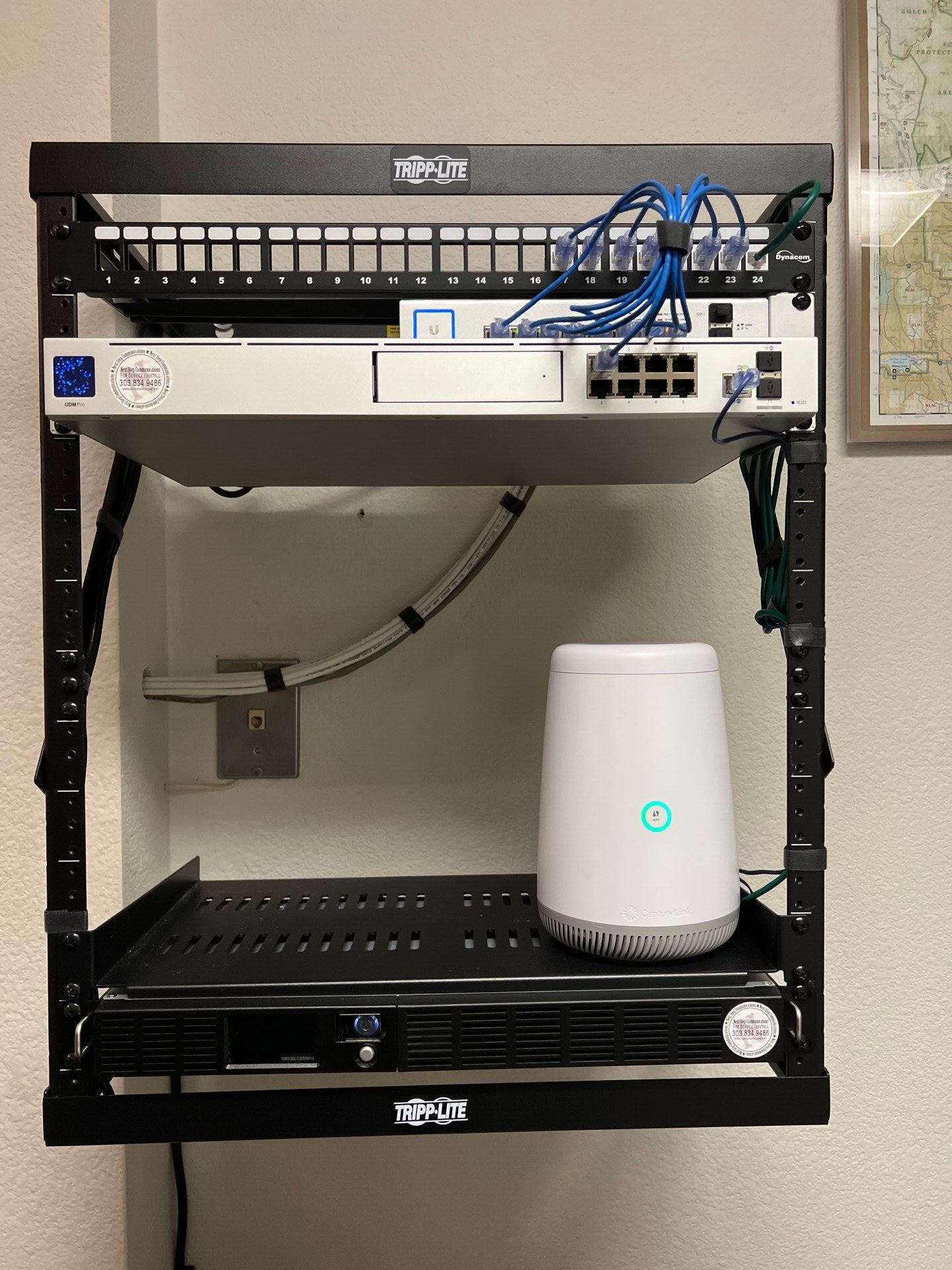 Wall-mounted network rack with a white router and blue cables in a room.
