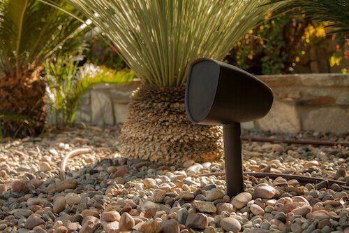 Black garden spotlight among pebbles beside a spiky plant and stone wall