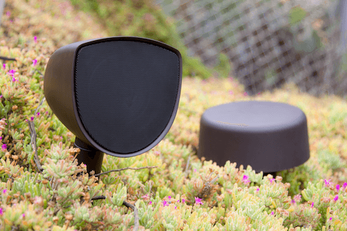 Two black speaker-like objects on mossy ground, one upright and one lying flat, outdoors.