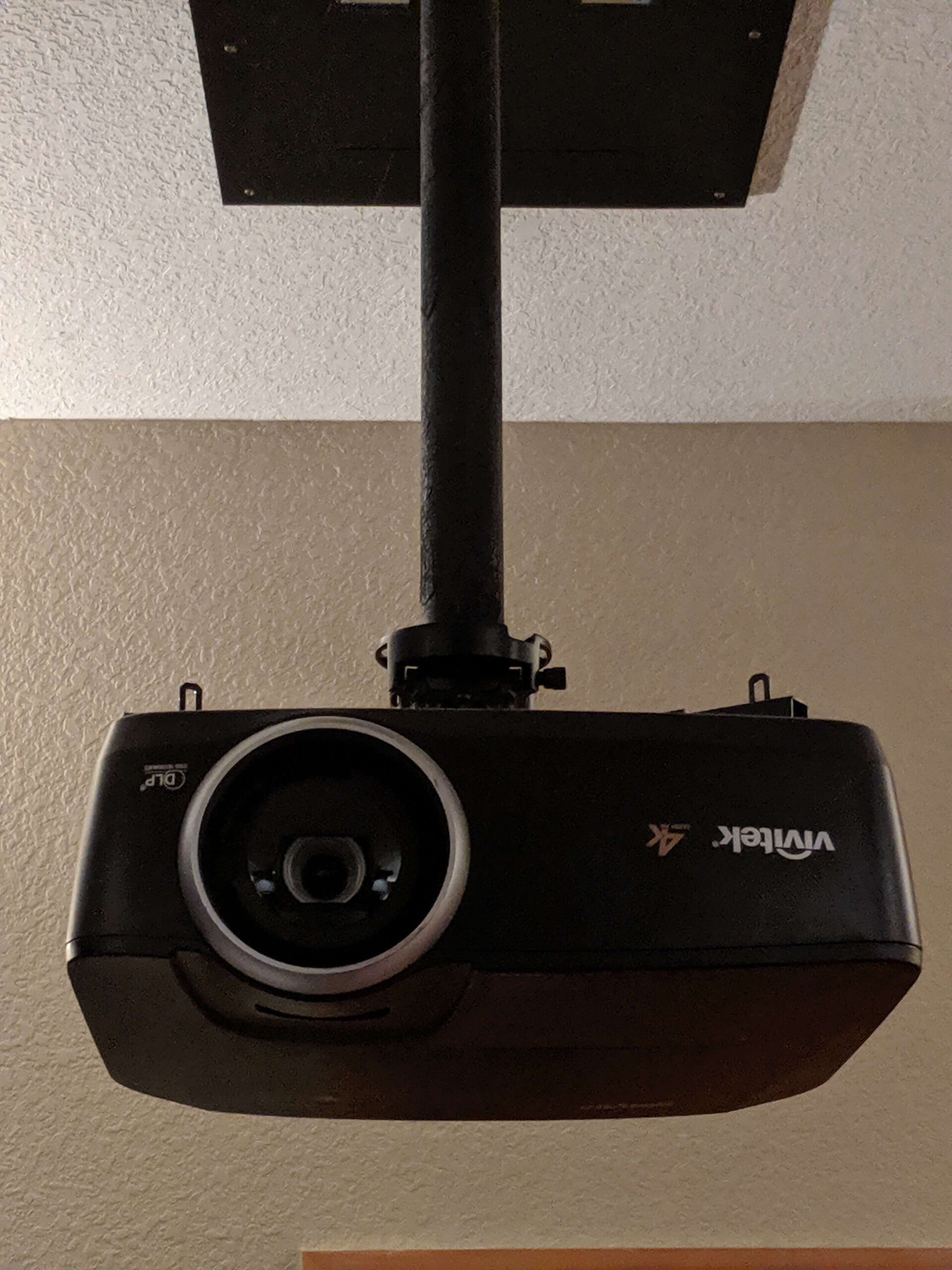 Ceiling-mounted black projector hanging from a pole, facing downward.