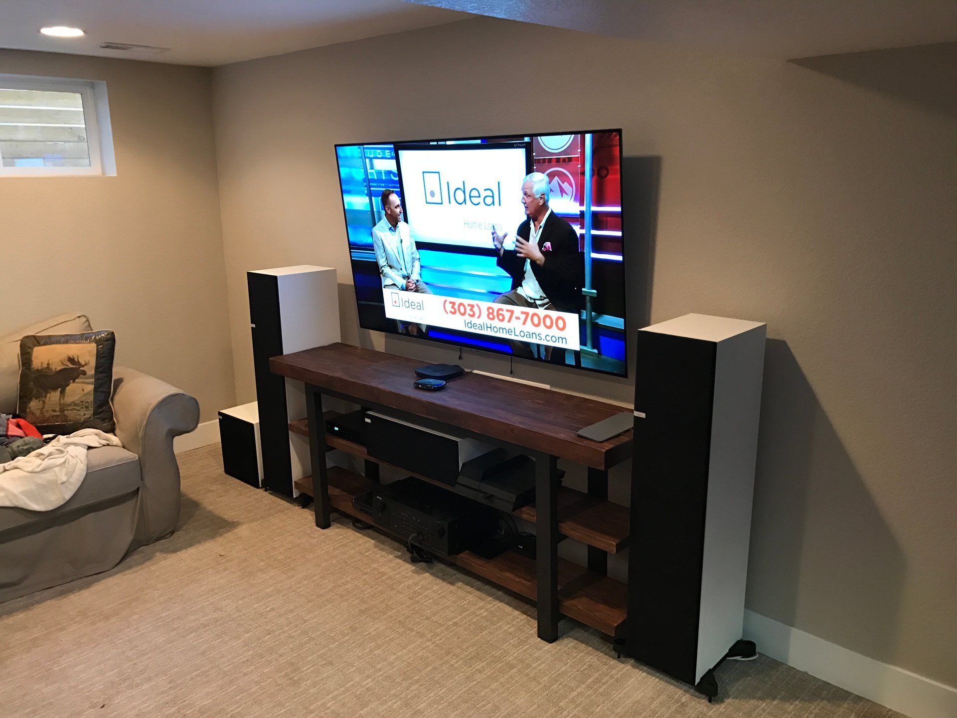 Living room with TV on a stand between two tall speakers, beige couch, and carpeted floor