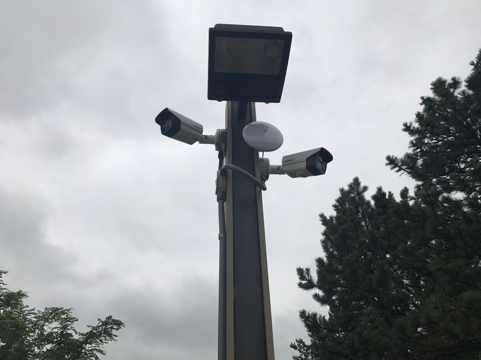 Security cameras and a solar panel mounted on a pole against an overcast sky.
