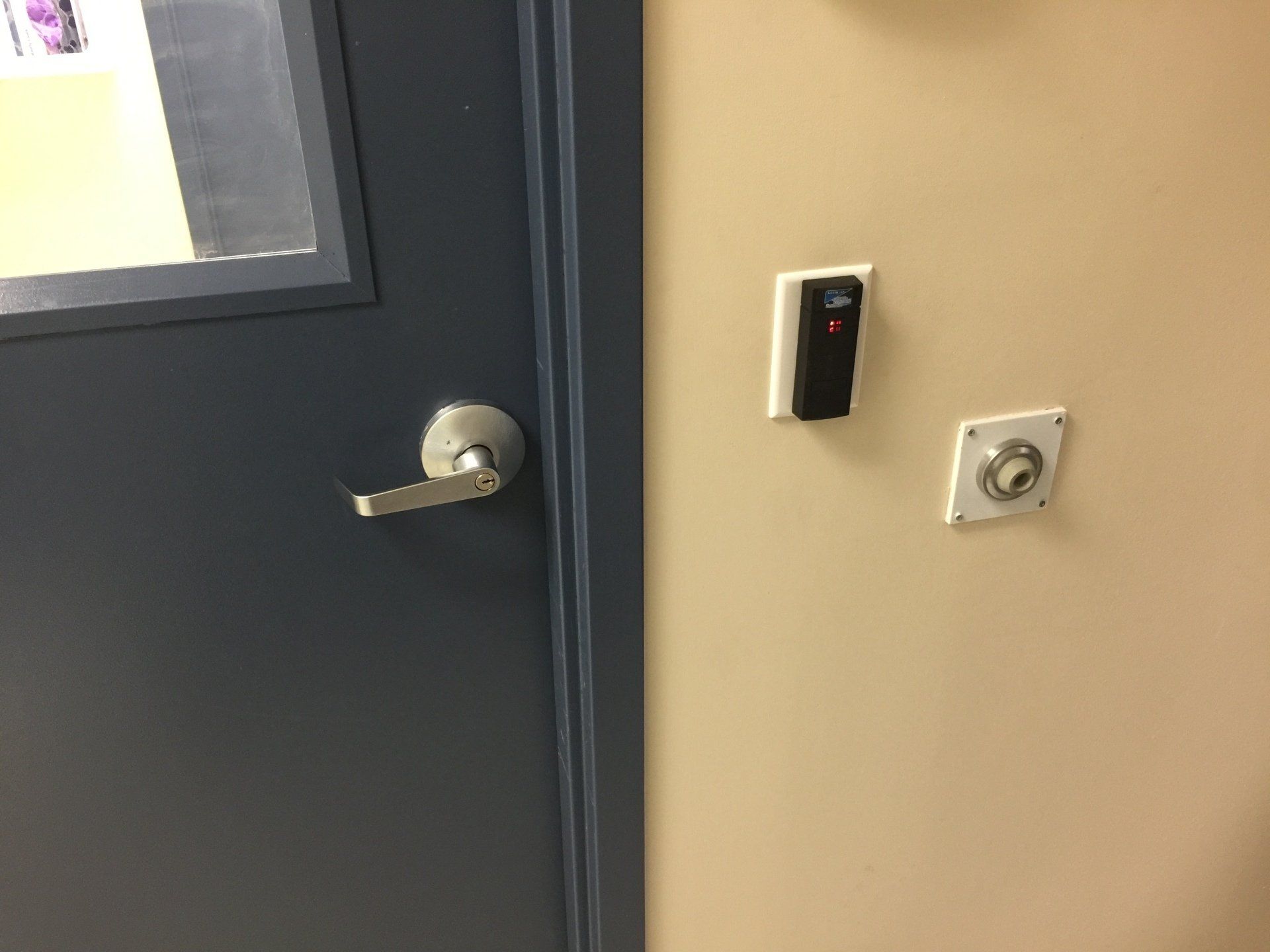 Blue door with handle beside wall-mounted access buttons and a small control panel