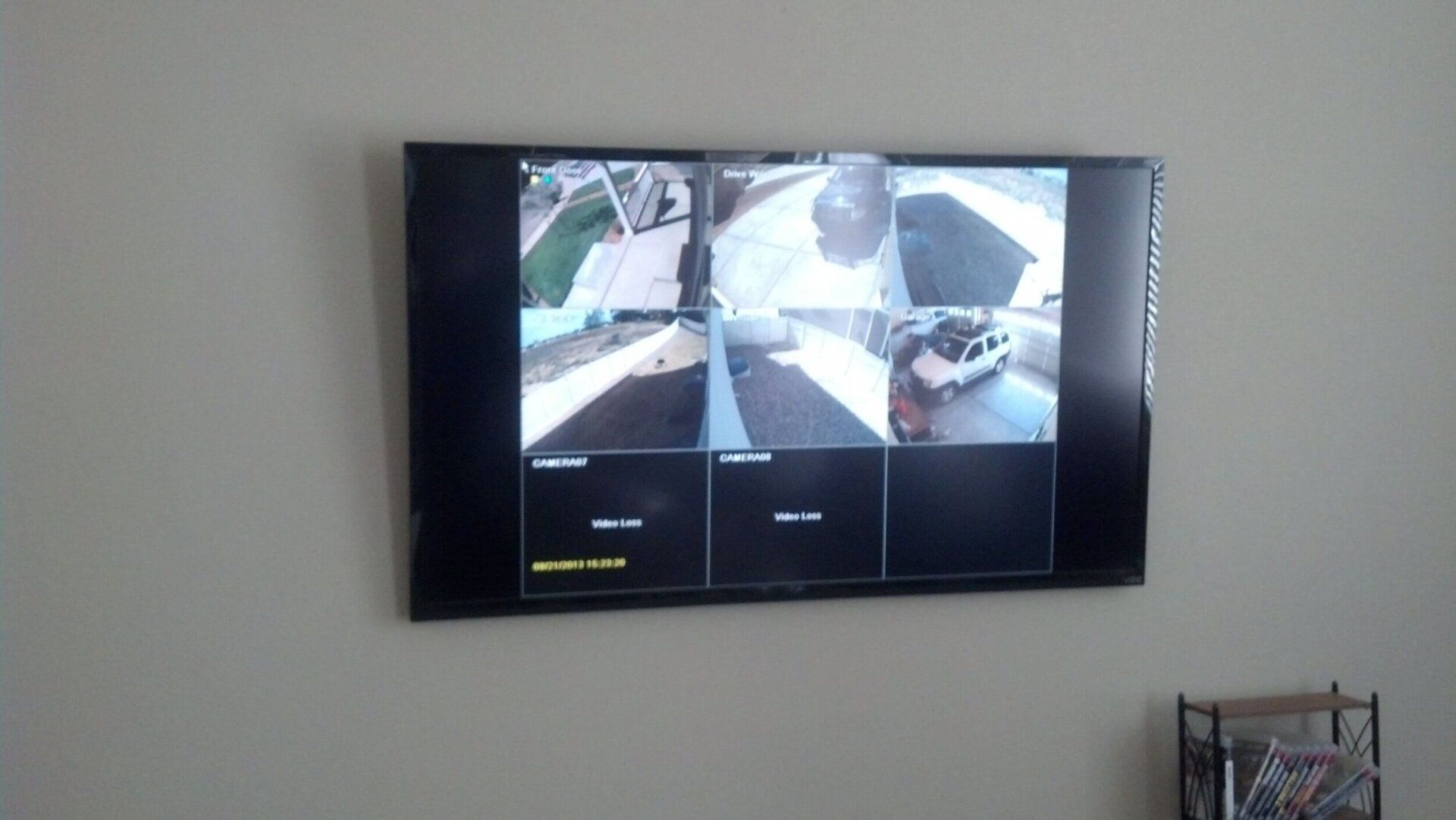 Wall-mounted TV showing a multi-camera security monitor in a plain room