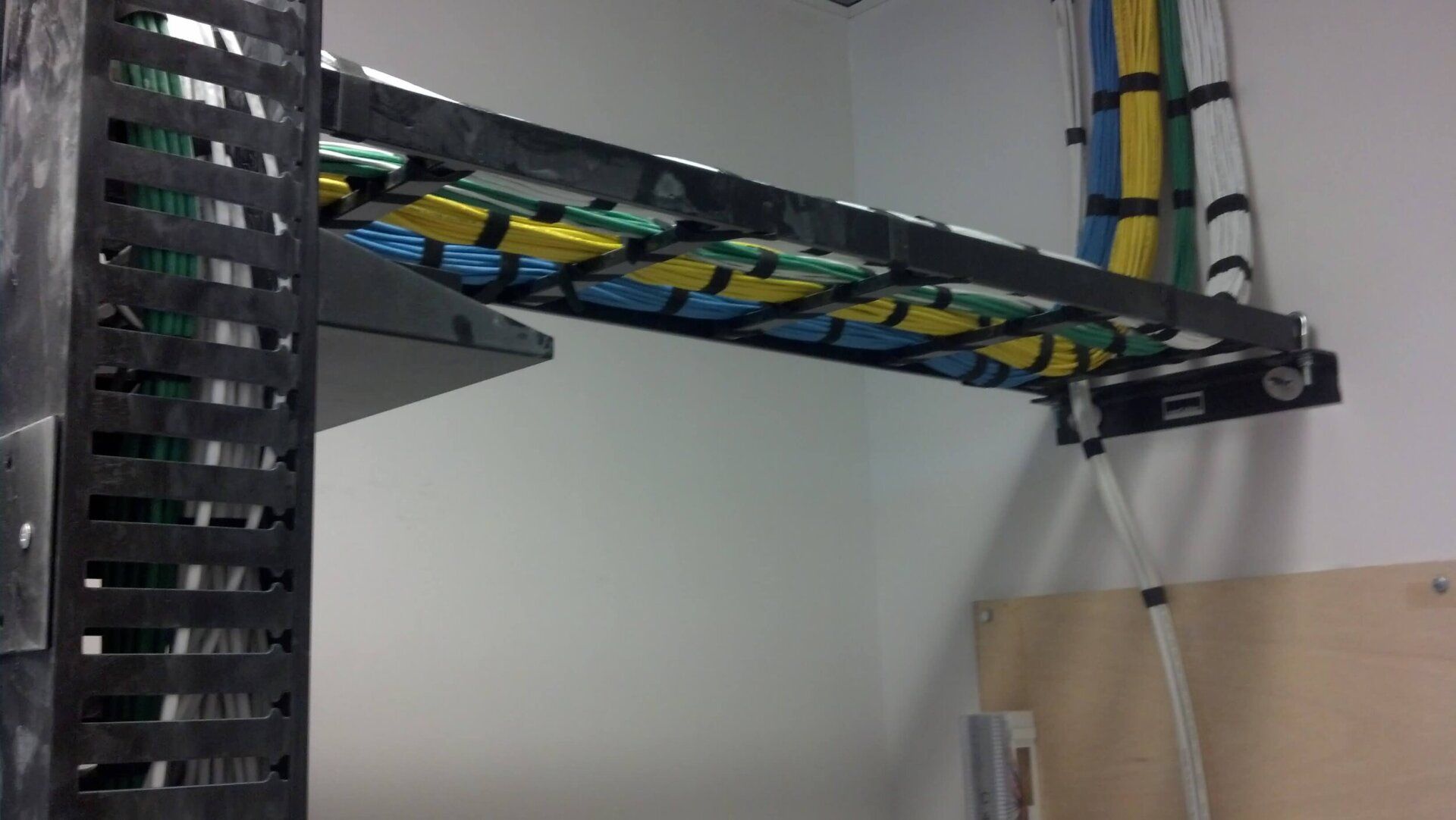Network cables routed through a black cable tray and vertical cable organizer on a wall-mounted rack.