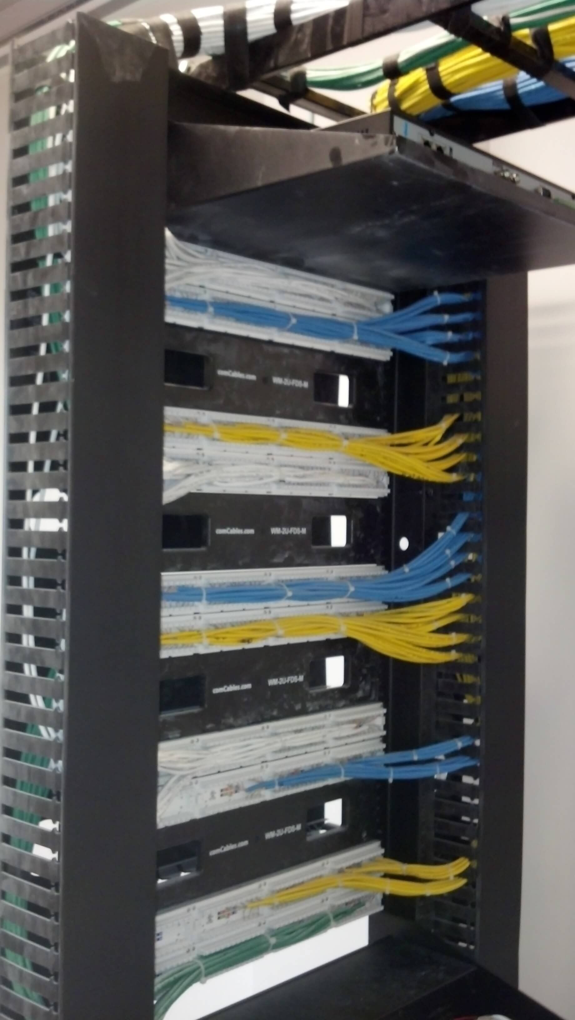 Network rack with neatly organized blue, yellow, and white Ethernet cables connected to patch panels