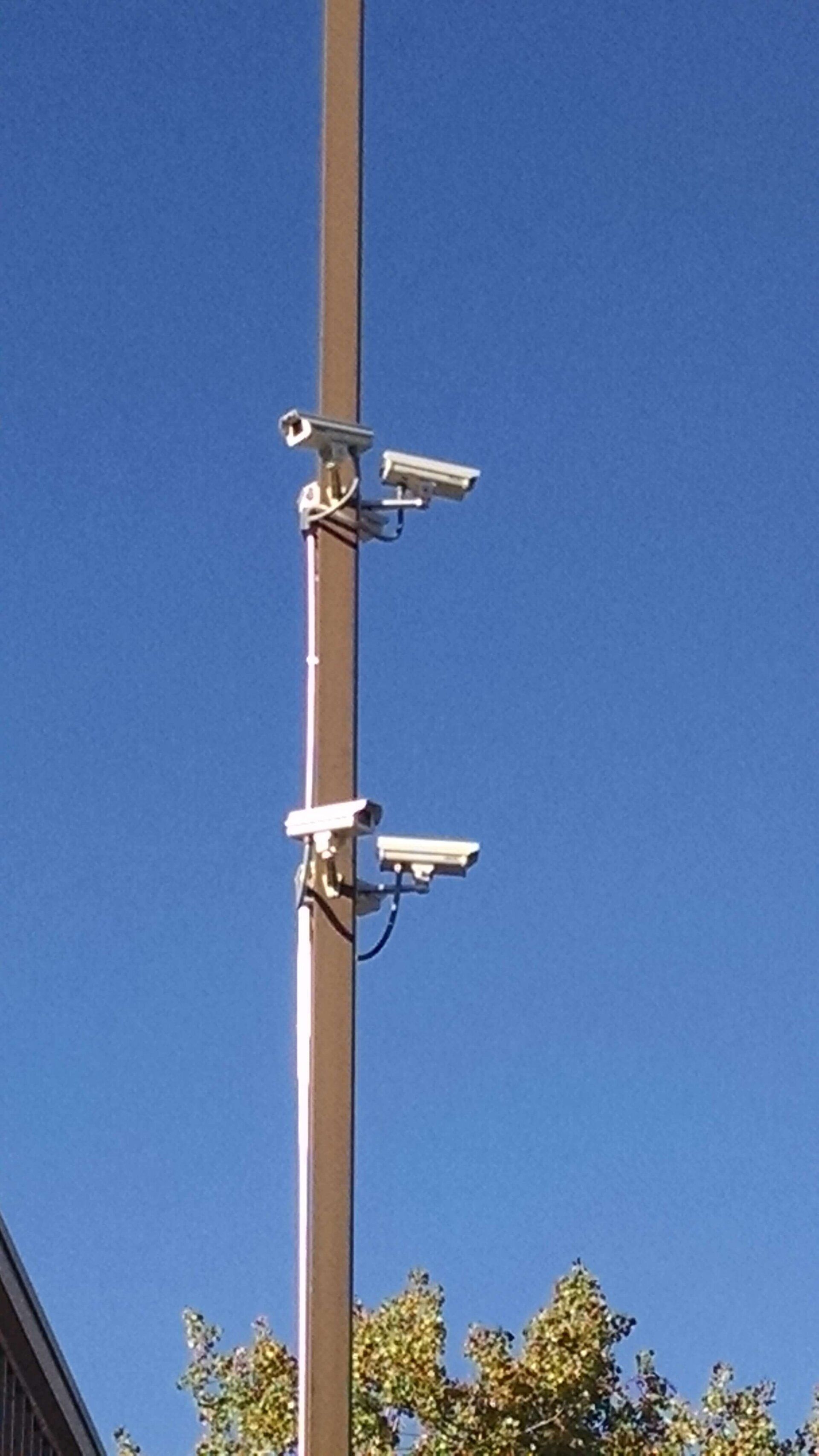 Two security cameras mounted on a tan pole against a clear blue sky.