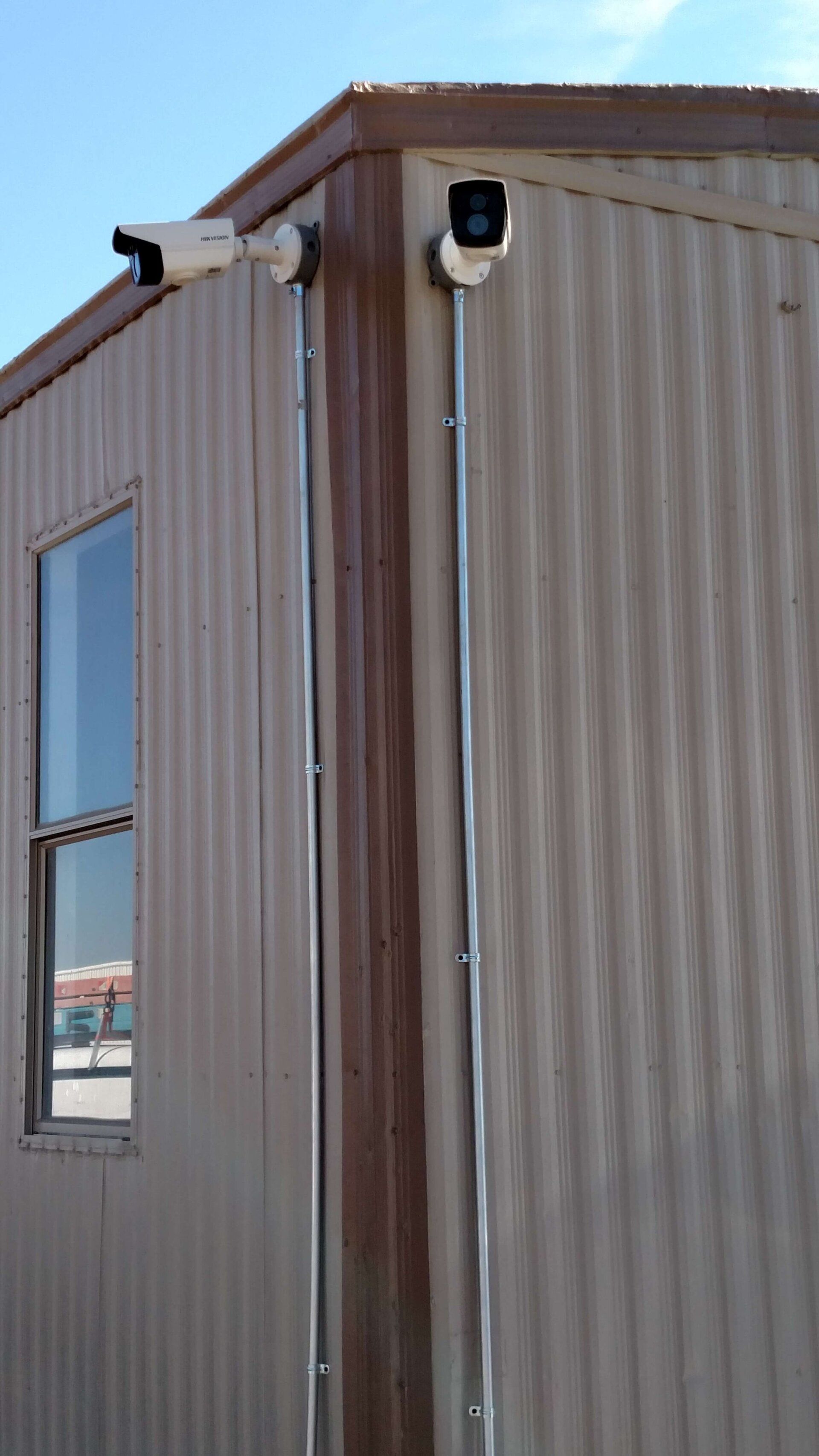 Corner of a beige metal building with windows and mounted security cameras.