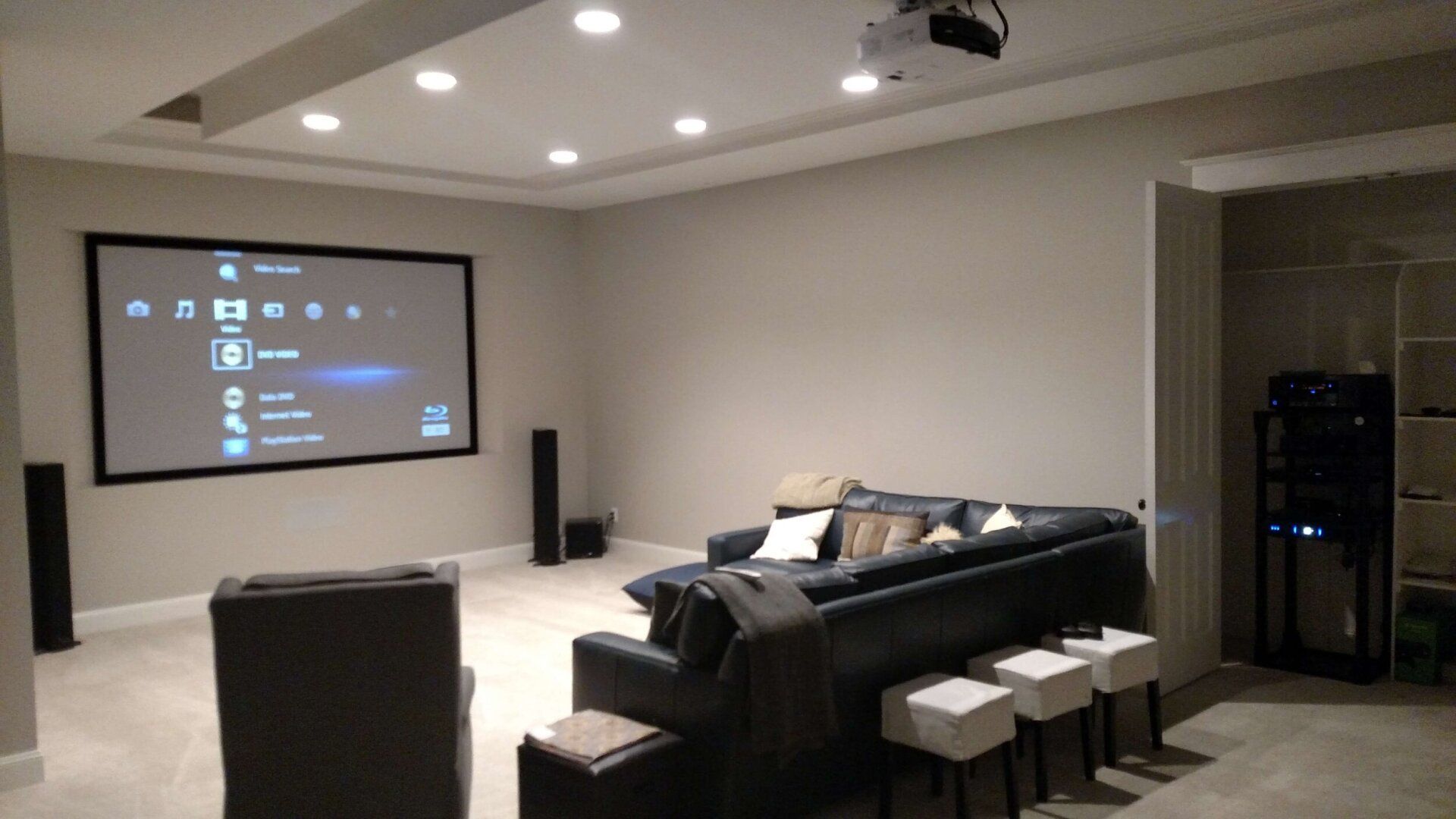 Modern home theater with projector screen, black sectional sofa, and recessed ceiling lights