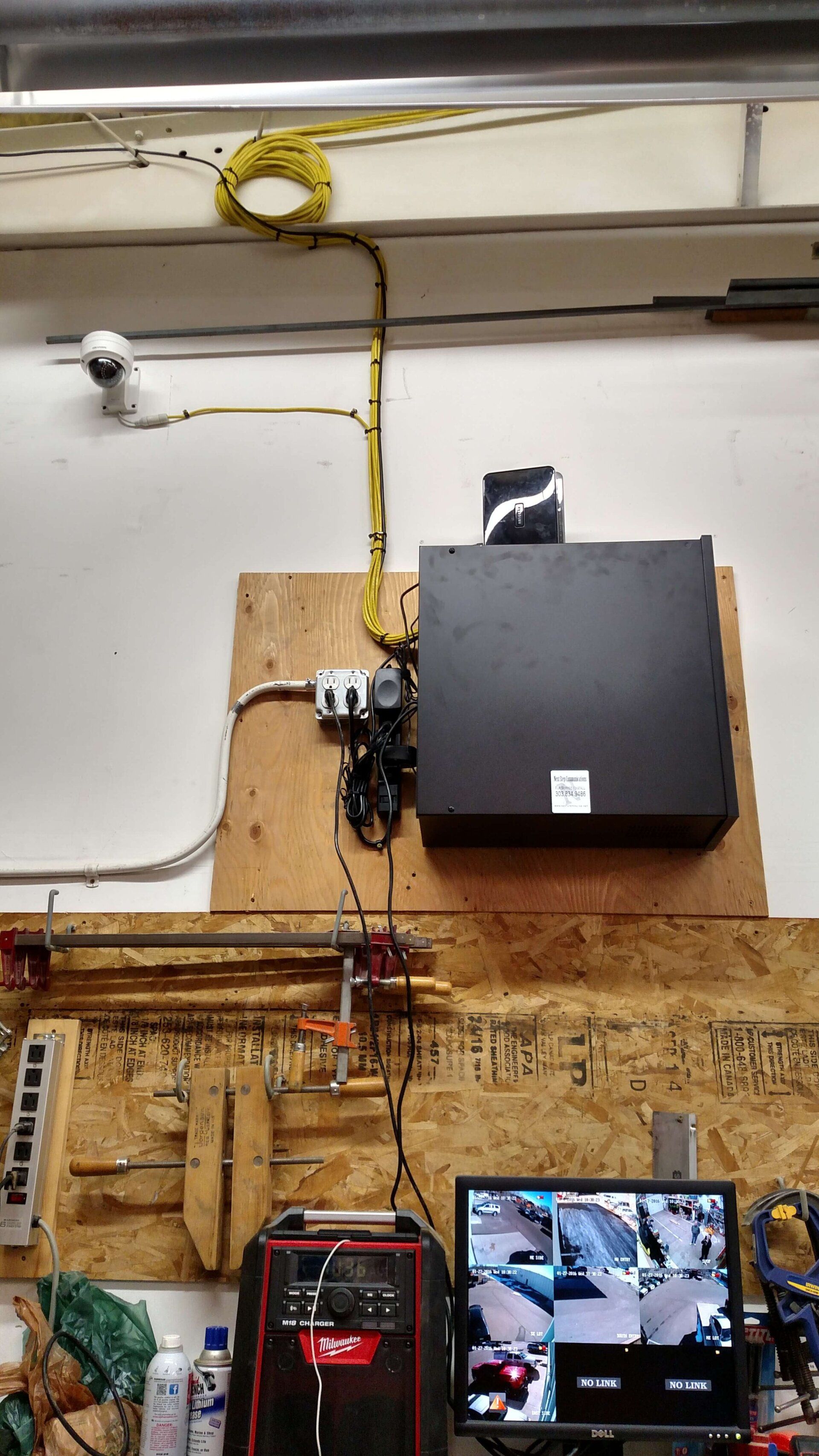 Workshop wall with mounted black monitor, wiring, and two small screens below displaying security camera views