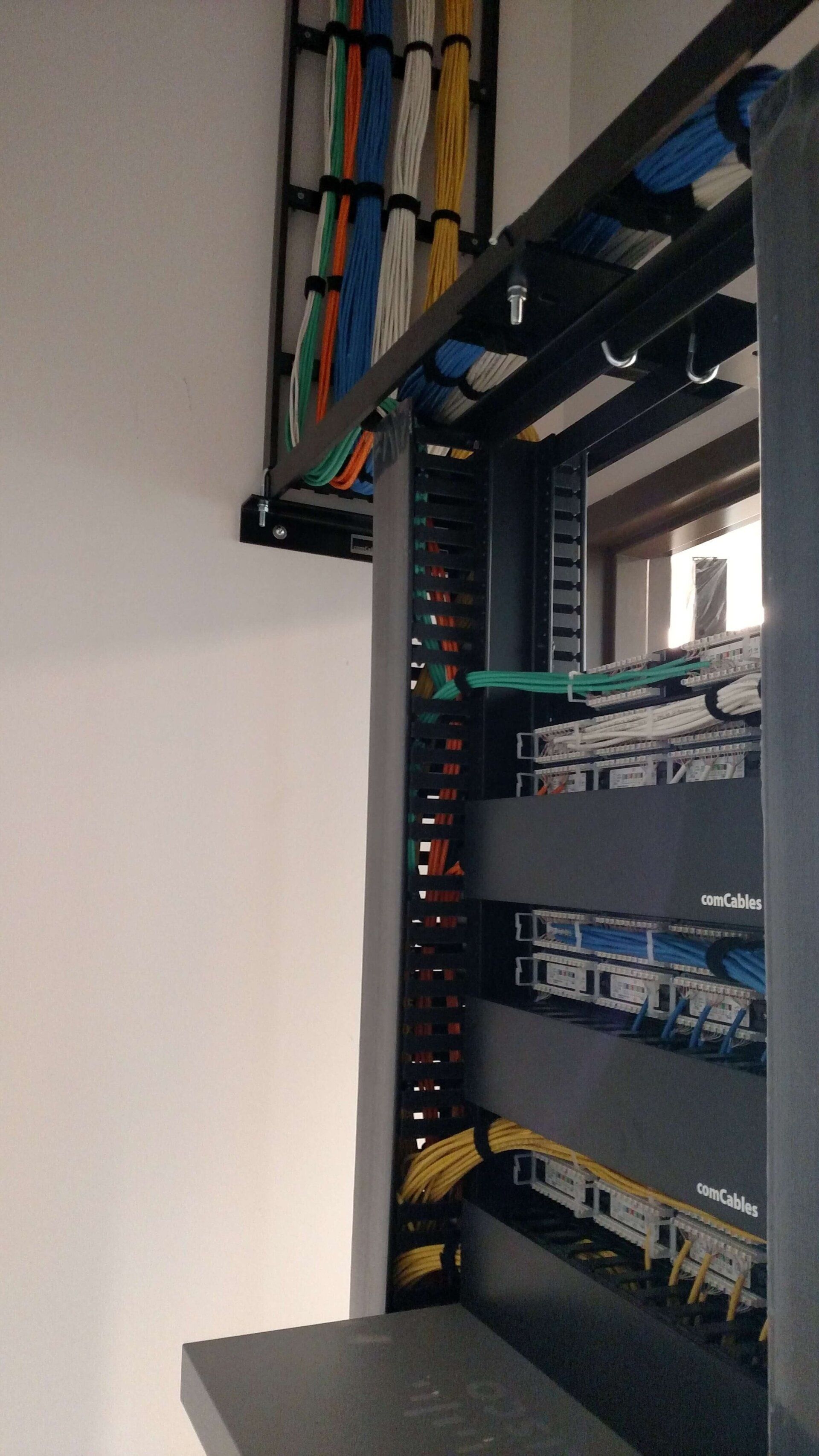 Open network rack with patch panels, switches, and bundled cables mounted on a wall.