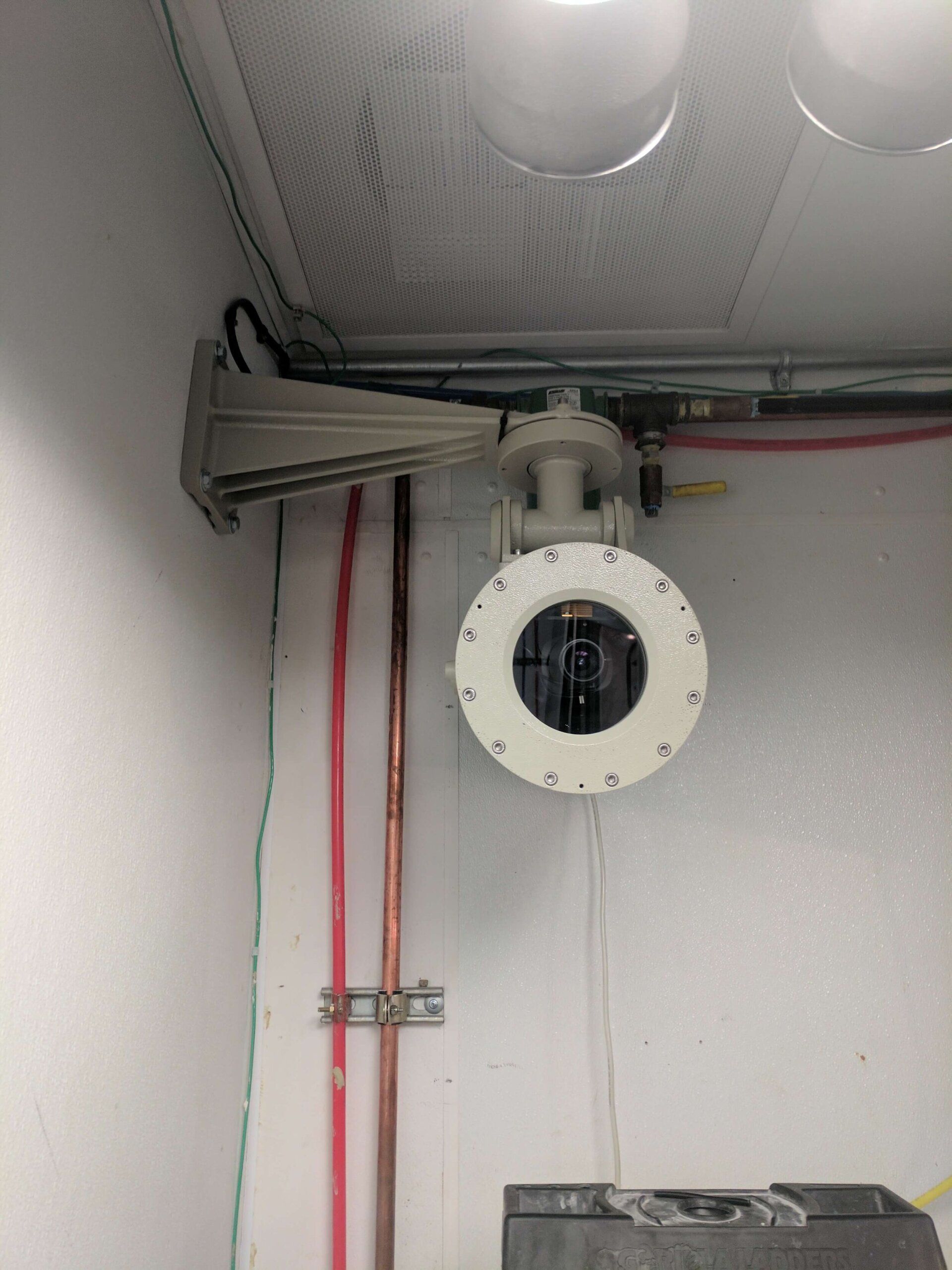 Wall-mounted industrial sensor or camera with cables in a utility room.