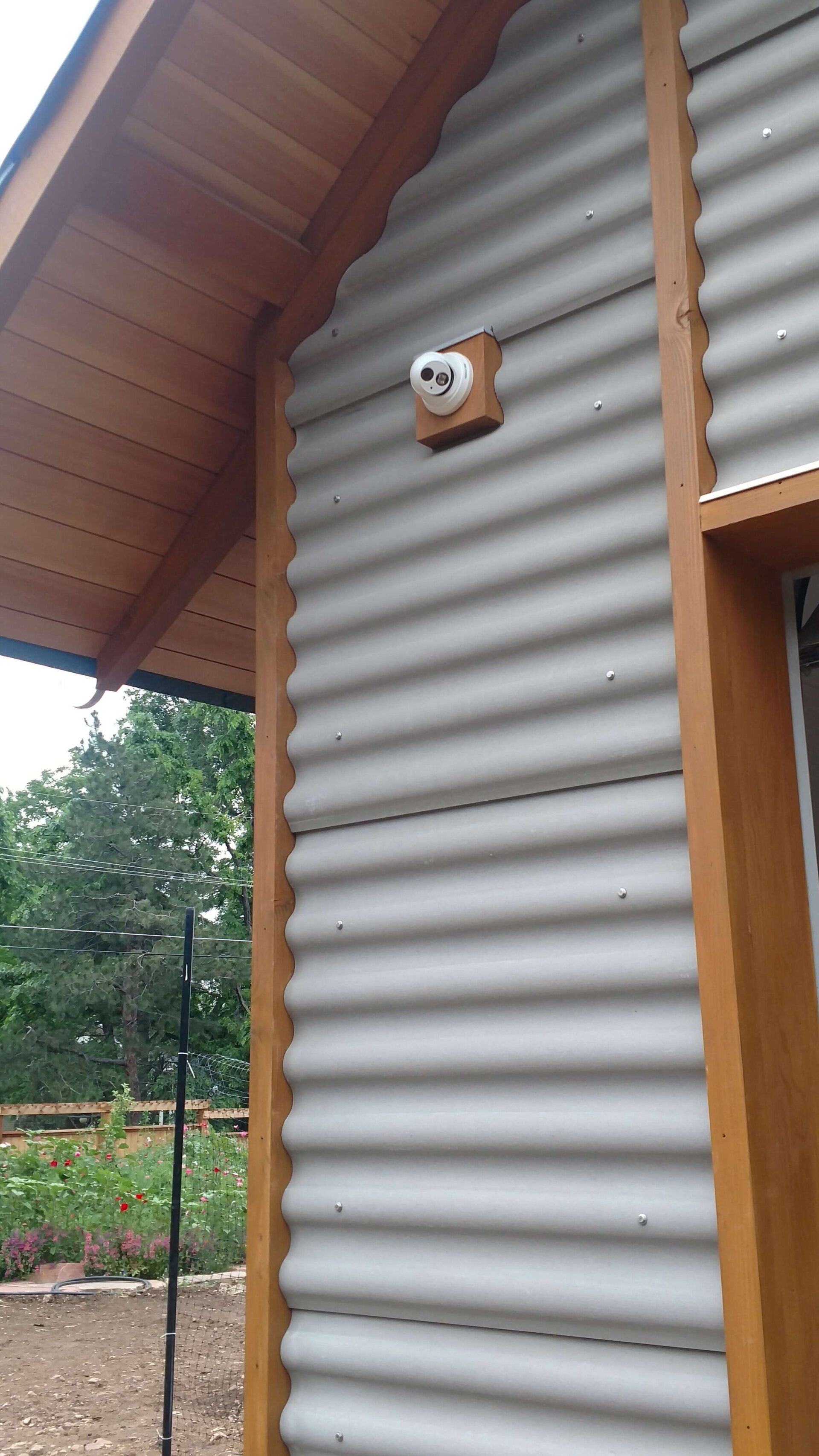 Exterior of a building with corrugated metal siding, wooden roof eaves, and a small wall-mounted light.