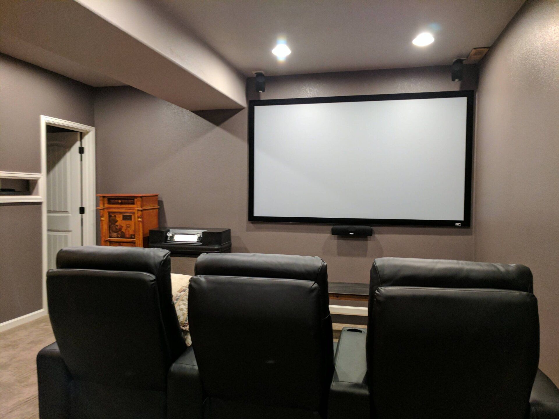 Home theater room with three black recliners facing a large projection screen