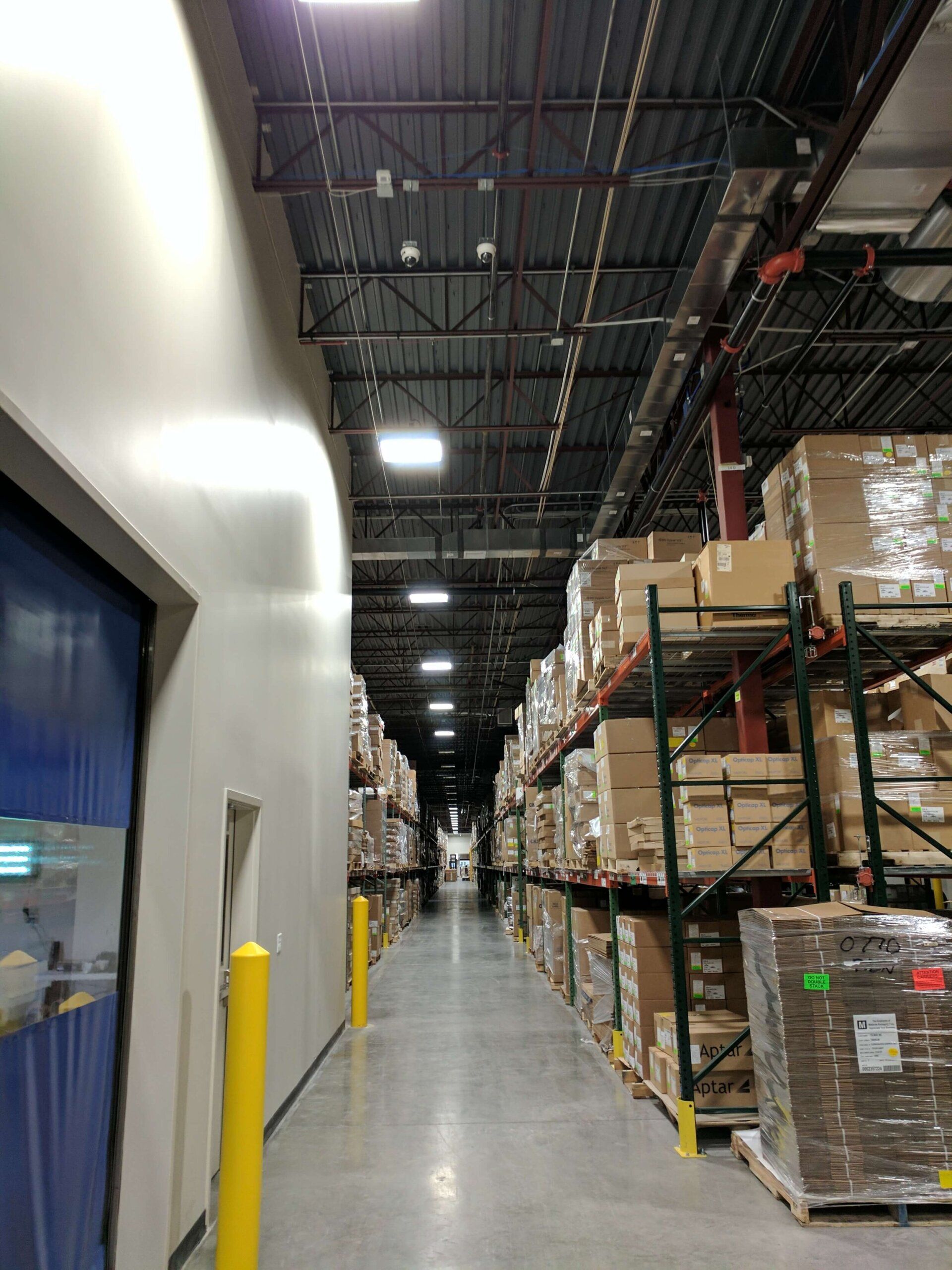 Warehouse aisle with tall shelves of stacked boxes beside a blue wall and concrete floor