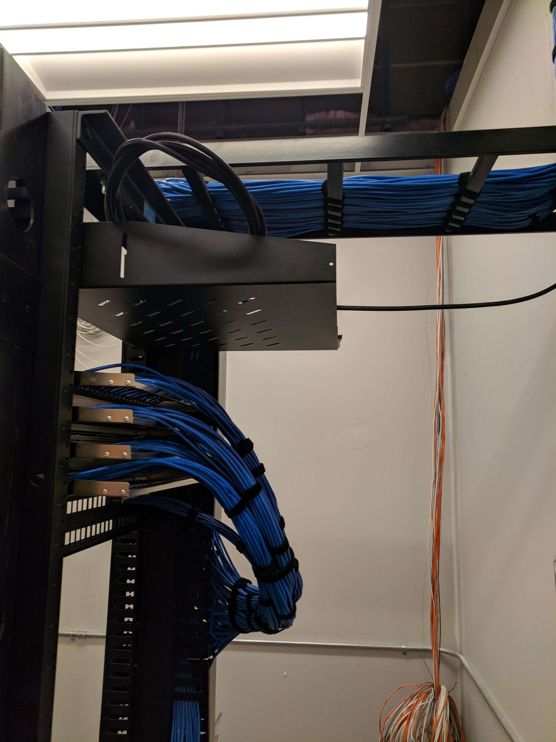 Network cabinet with blue ethernet cables neatly routed on black shelves in a small server closet
