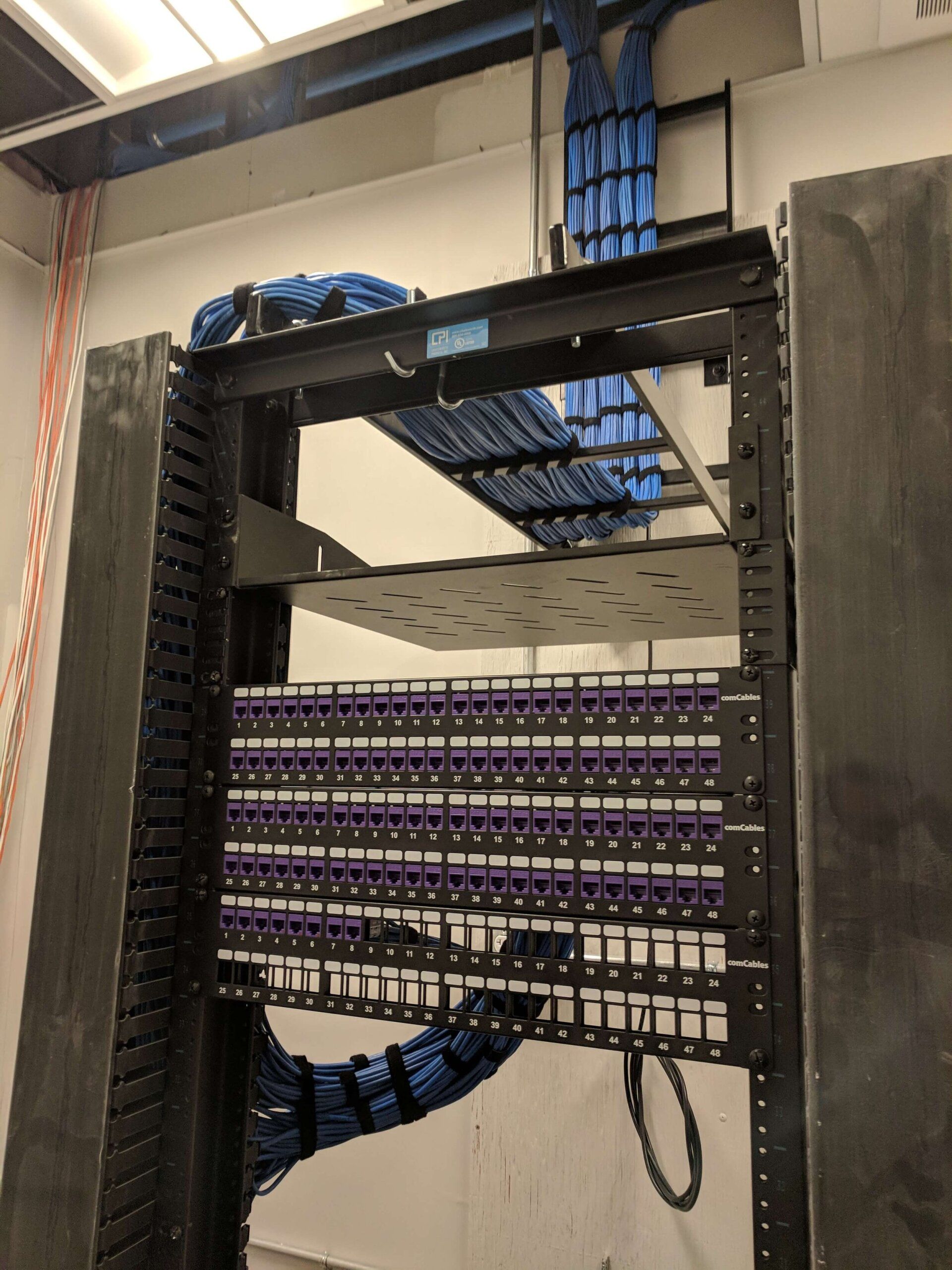 Network rack with rows of purple patch panels and blue cable bundles in a server room