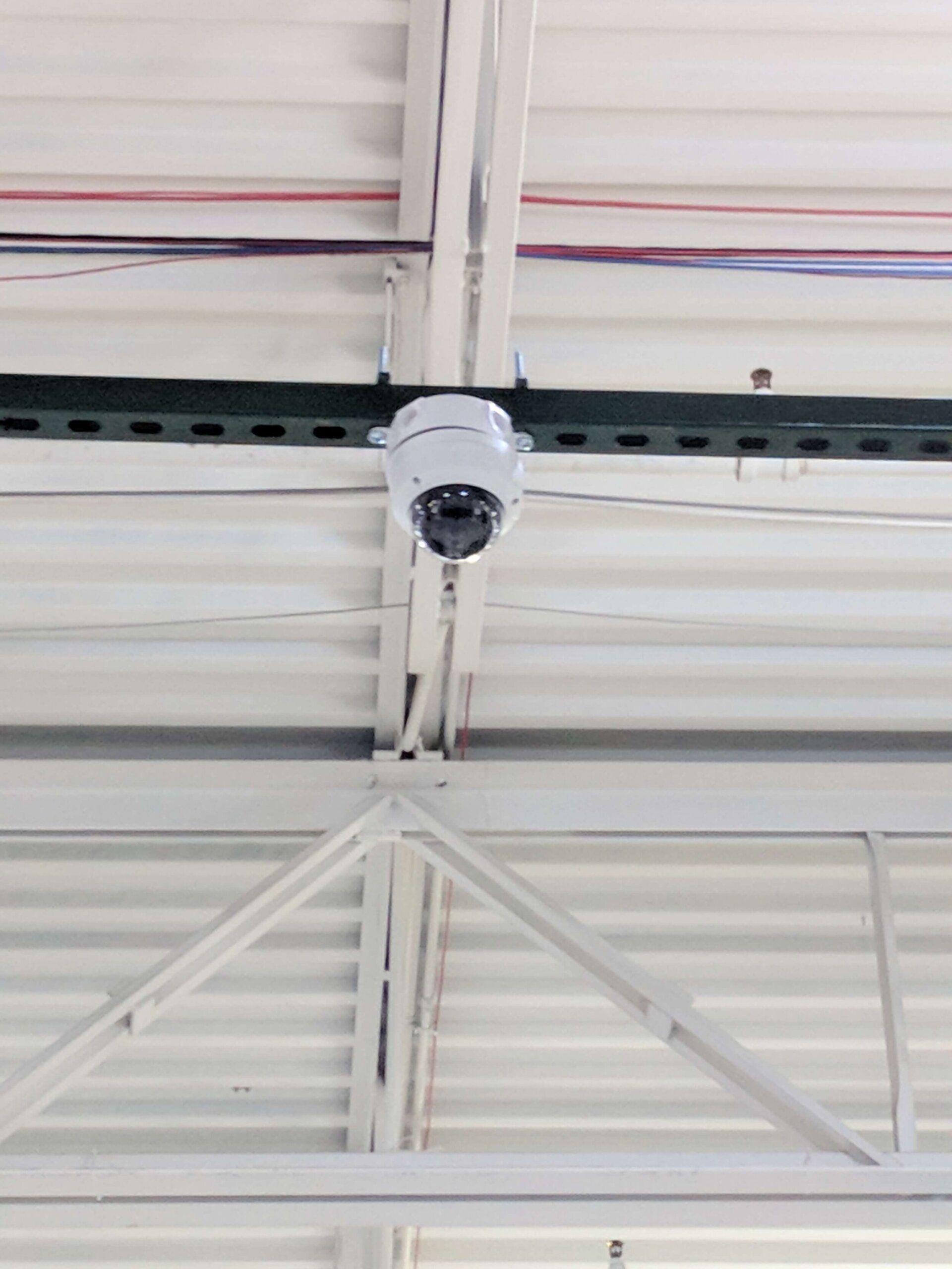Ceiling-mounted security camera on a white industrial ceiling with beams and wiring