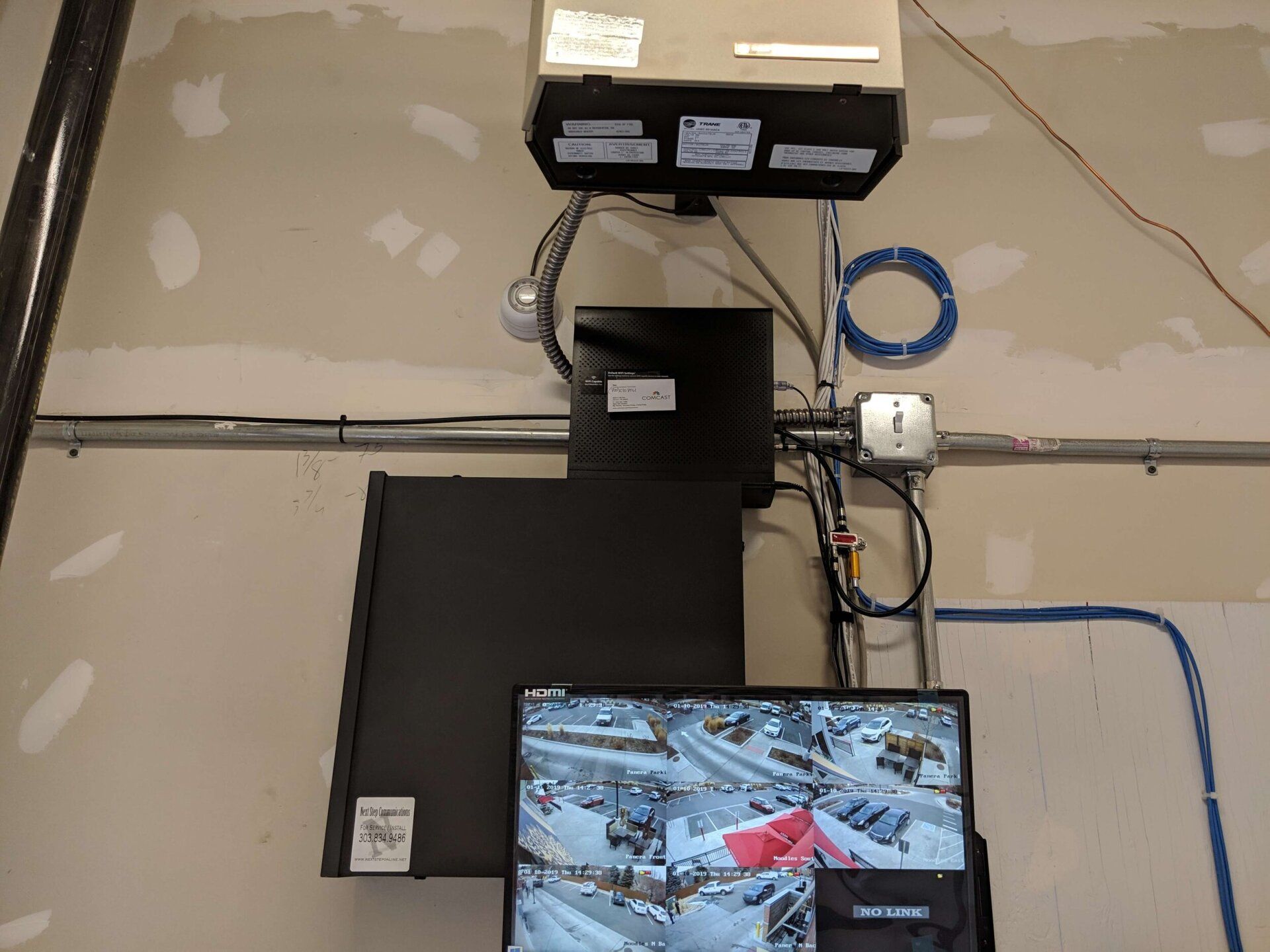 Ceiling-mounted surveillance equipment with cables and a small monitor showing a parking lot