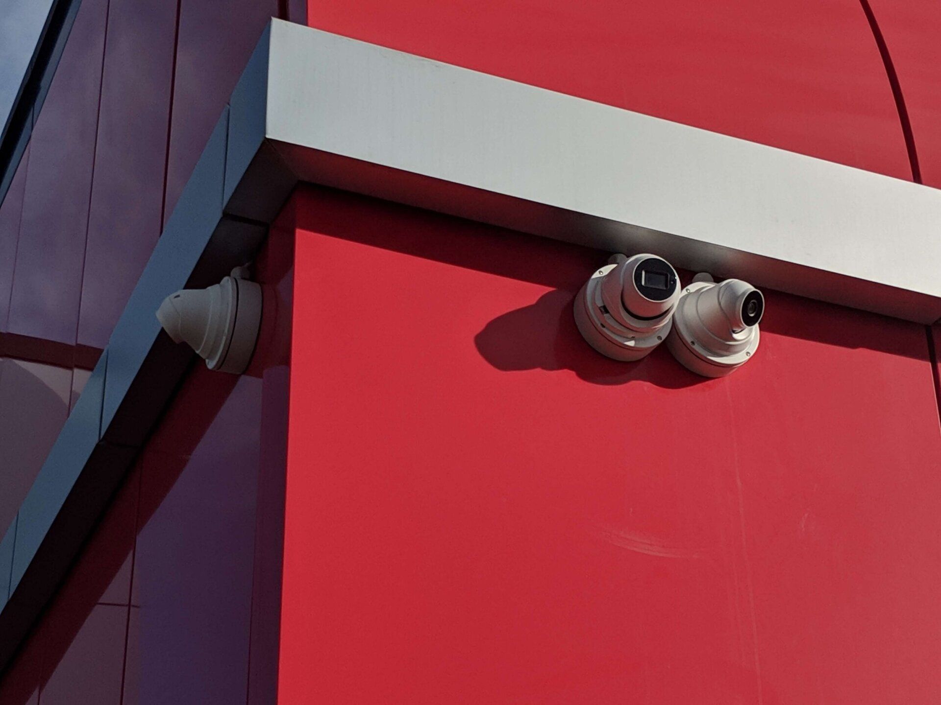 Red building corner with white trim and two security cameras mounted on the wall