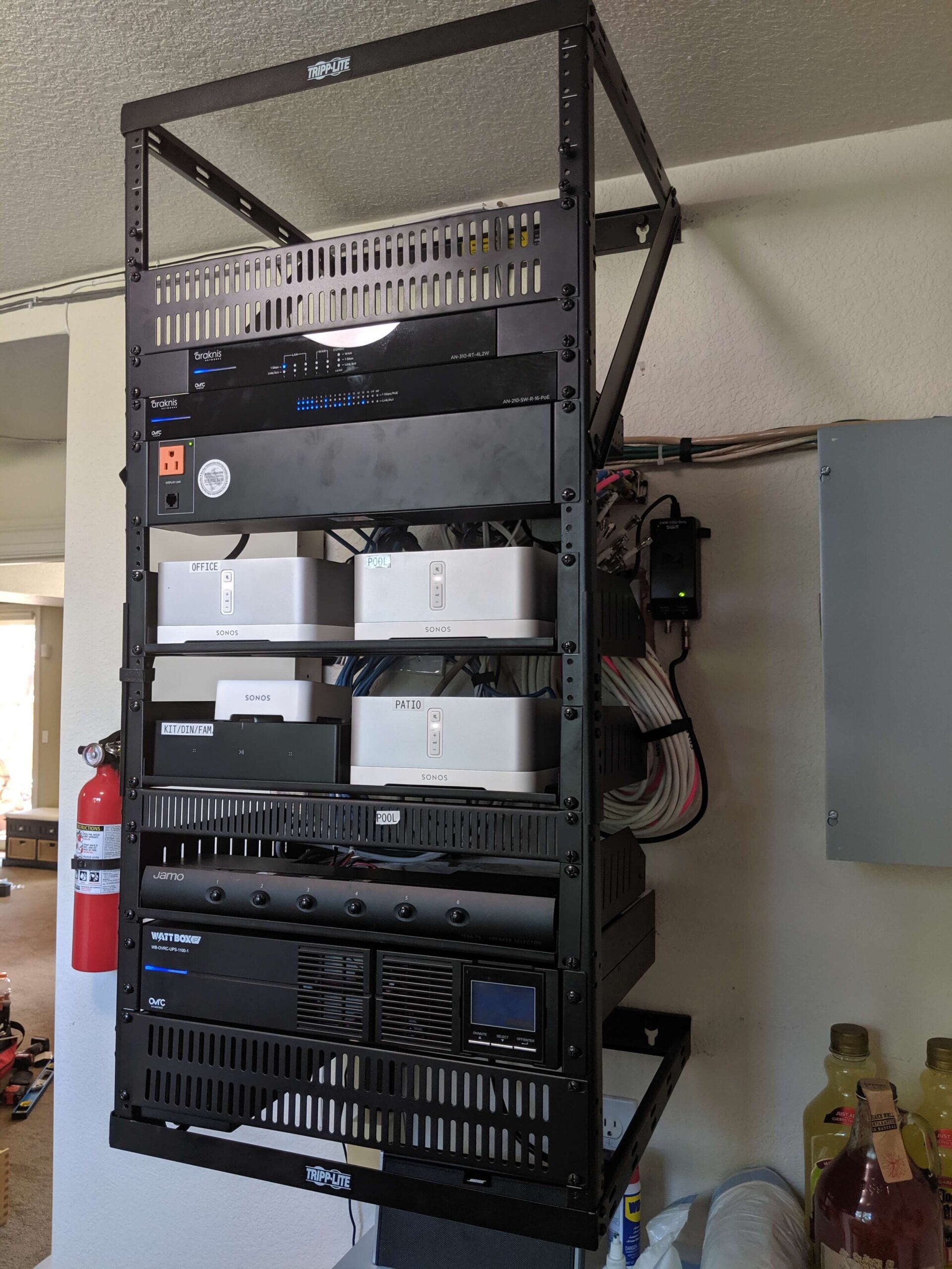 Wall-mounted black server rack with network equipment and cables in a room