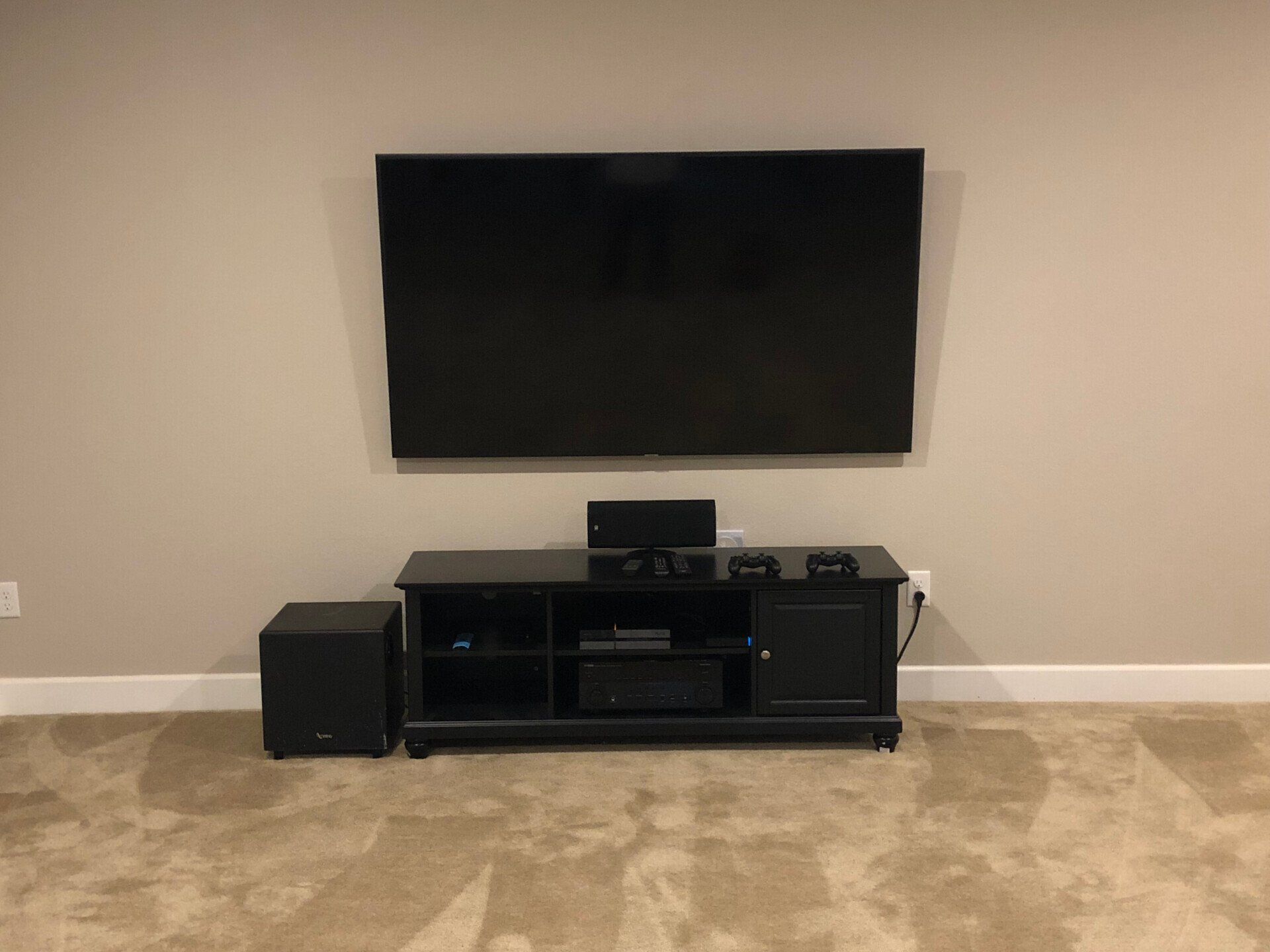 Wall-mounted TV above a black media console in a beige-carpeted living room.
