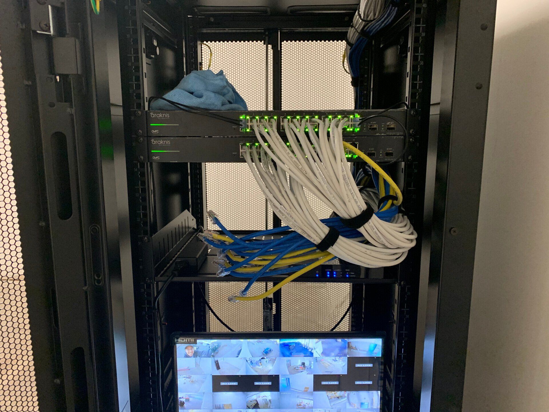 Server rack with bundled network cables and a small monitor displaying a desktop interface